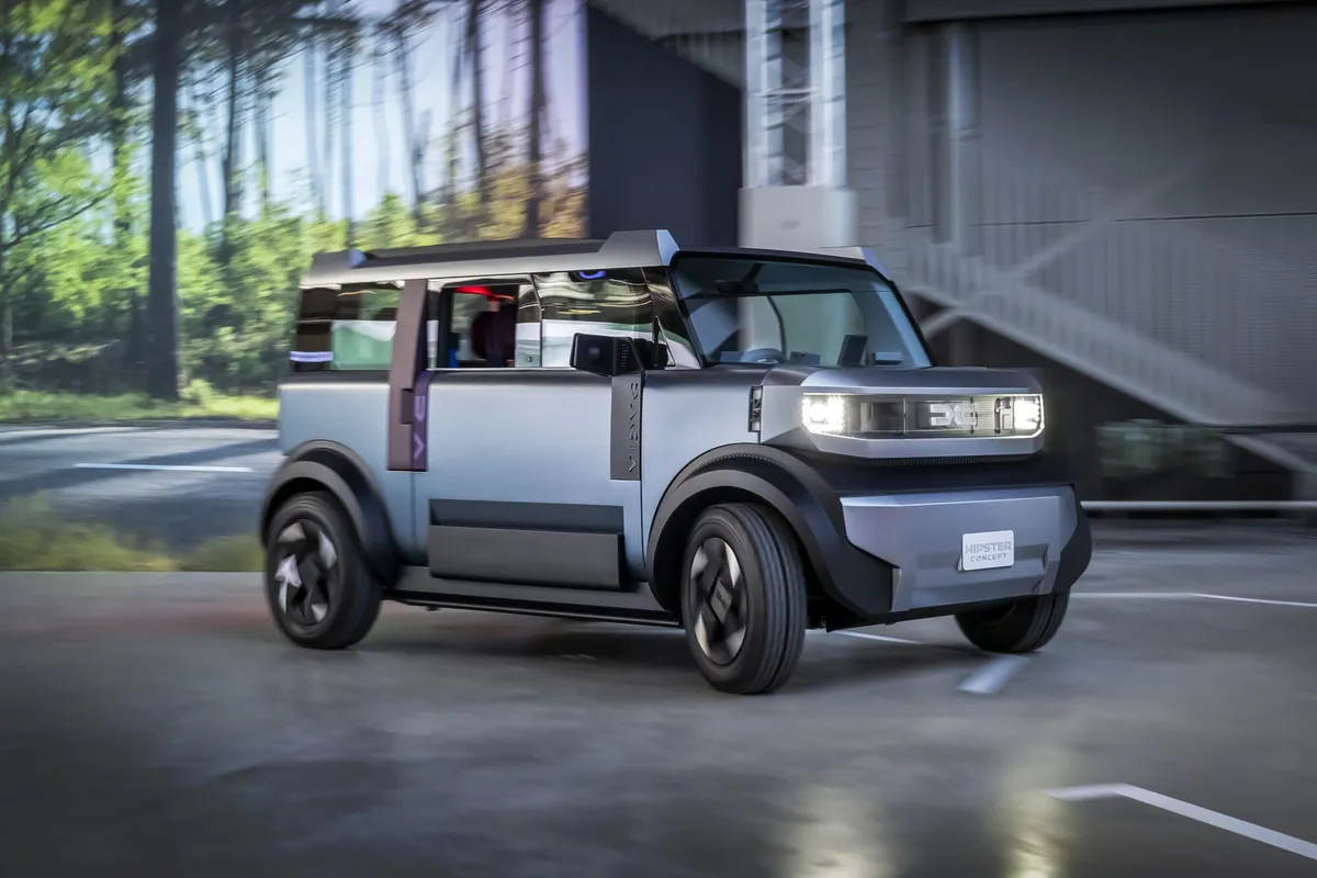 Hellgraues Dacia Hipster Concept mit violetten Akzenten von schräg vorne vor einem modernen Gebäude, dahinter Bäume.