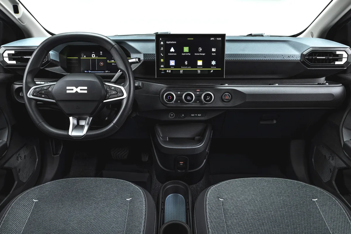 Innenraum des Dacia Spring: Lenkrad mit Dacia-Logo, digitales Kombiinstrument, Zentraldisplay und Klimaregler.