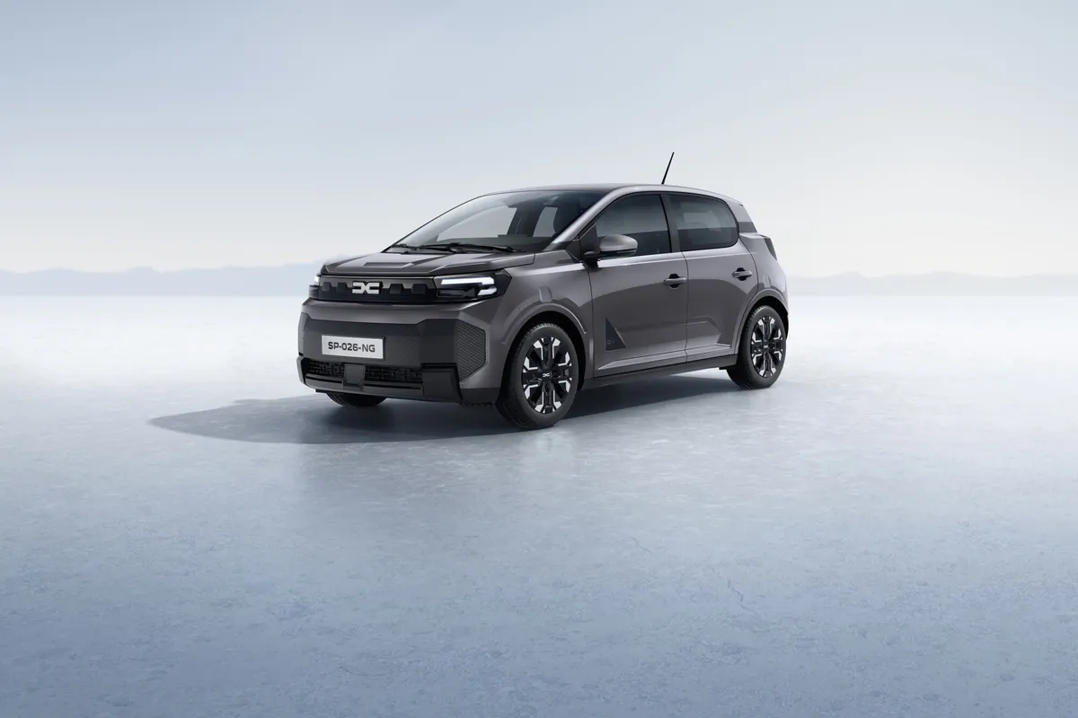 Dunkelgrauer Dacia Spring von schräg vorne auf einer hellen, weiten Fläche vor blassblauem Horizont.