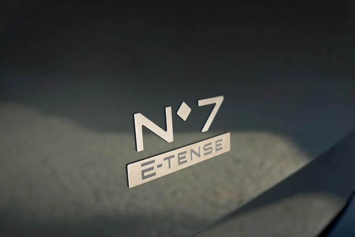 Nahaufnahme des Schriftzugs N°7 E-TENSE auf der graugrünen Karosserie eines DS N°7, mit starkem Licht und Schatten.