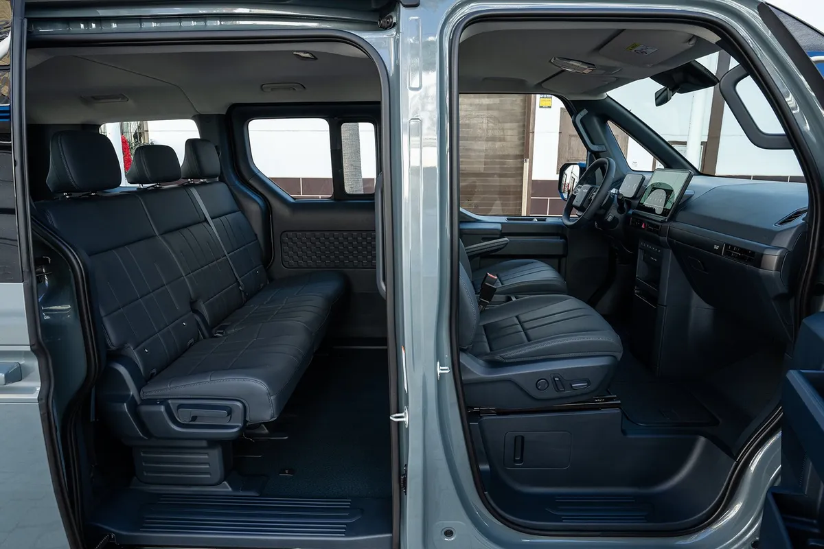Geöffnete Fahrer- und Schiebetür eines Kia PV5 Passenger mit Blick auf die dunklen Vordersitze und die dreisitzige Rückbank.