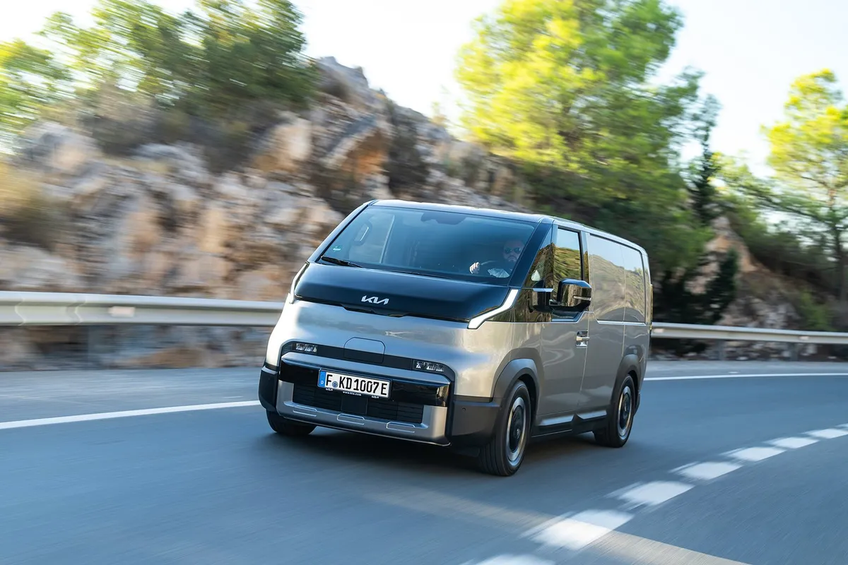 Grauer Kia PV5 Cargo von schräg vorne in Fahrt auf einer Bergstraße mit Leitplanke.