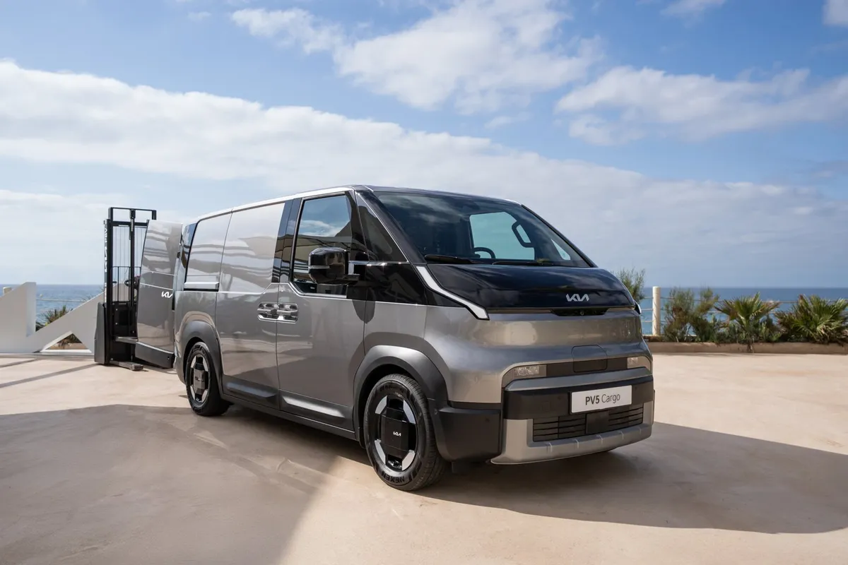 Grauer Kia PV5 Cargo von schräg vorne, geparkt auf einer Terrasse am Meer.