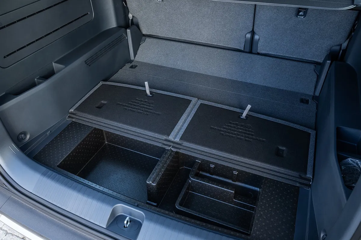Angehobene Bodenplatten im Kofferraum des Kia PV5 Passenger mit darunterliegenden Staufächern.