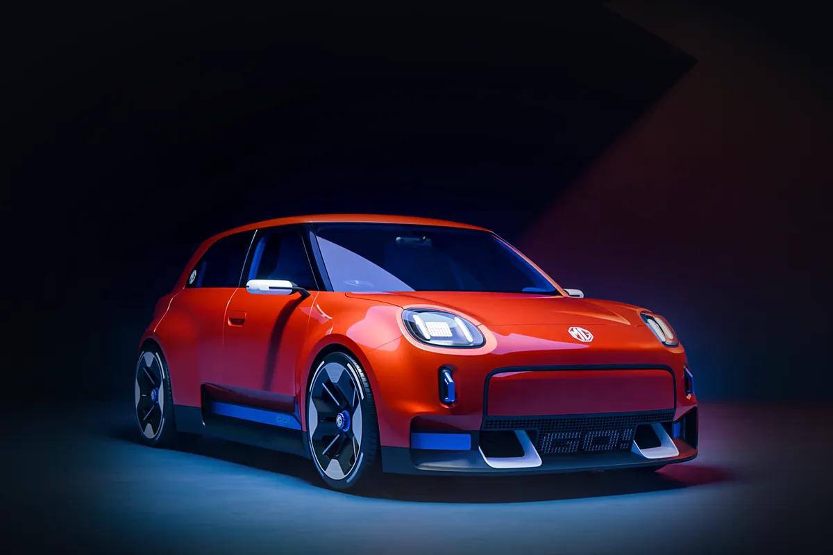 Oranges MG GO! Concept mit schwarzem Dach von schräg vorne im abgedunkelten Studio, das Auto im warmen Licht, darunter ein heller Lichtschein am Boden.