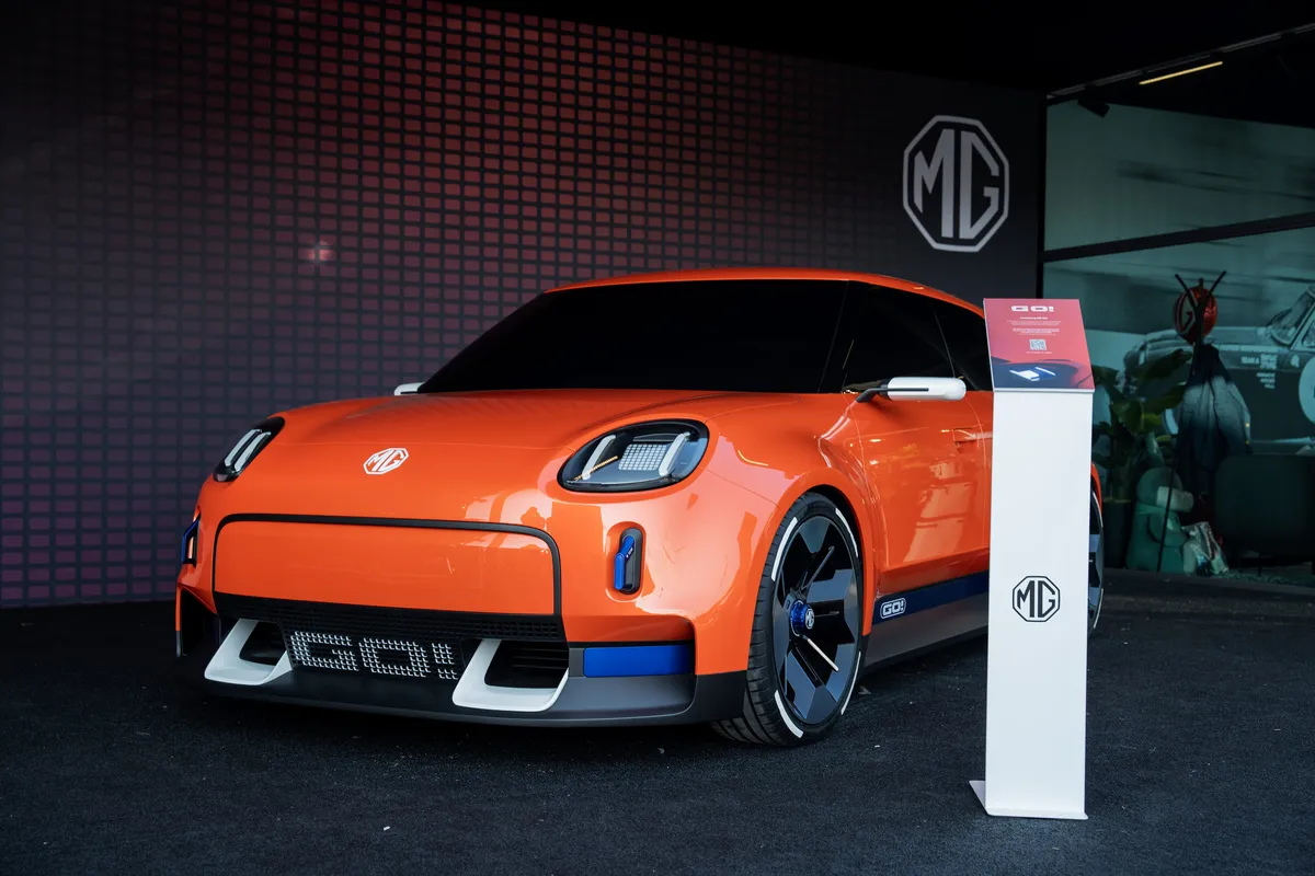 Oranges MG GO! Concept von schräg vorne auf dem dunklen MG-Messestand beim Goodwood Festival of Speed, daneben eine weiße Infosäule.