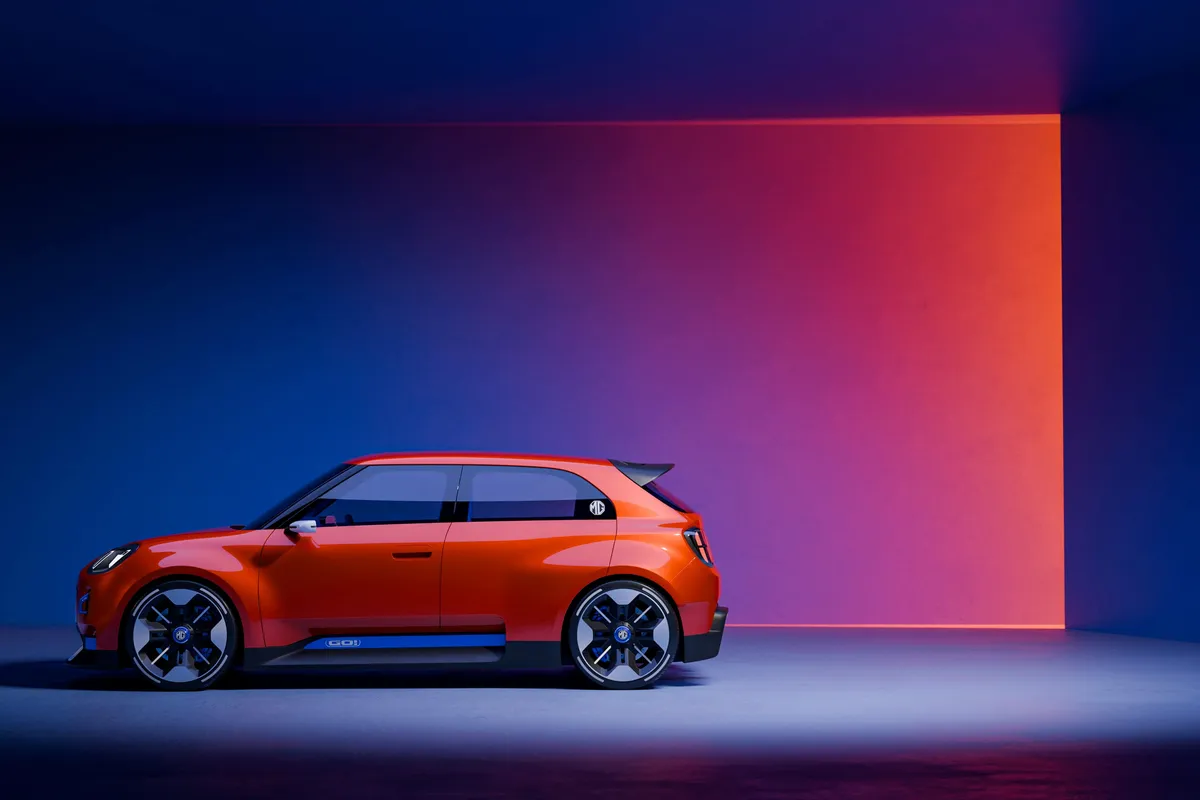 Oranges MG GO! Concept im Seitenprofil vor blauer Studiowand mit leuchtend orangem Lichtfeld, große schwarz-silberne Räder.