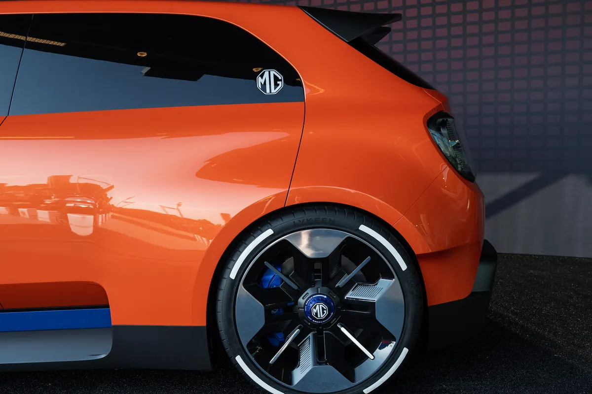 Hinterrad und hintere Seitenpartie des orangen MG GO! Concept auf dunklem Messeboden.
