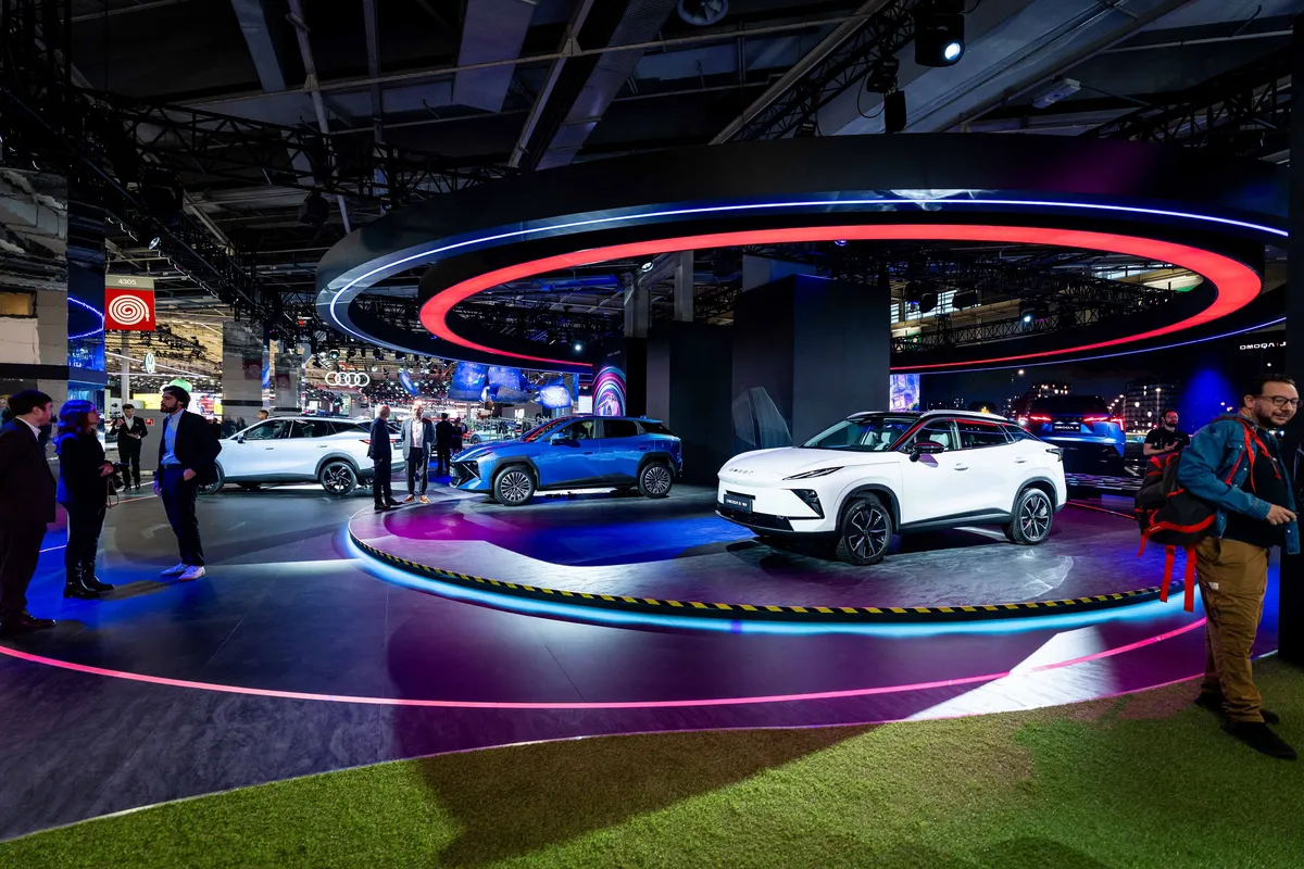 Messestand von Omoda und Jaecoo auf der Paris Motor Show mit beleuchteten Ringen an der Decke, vorne ein weißer Omoda 5, dahinter der blaue Omoda 4, dazwischen Besucher.