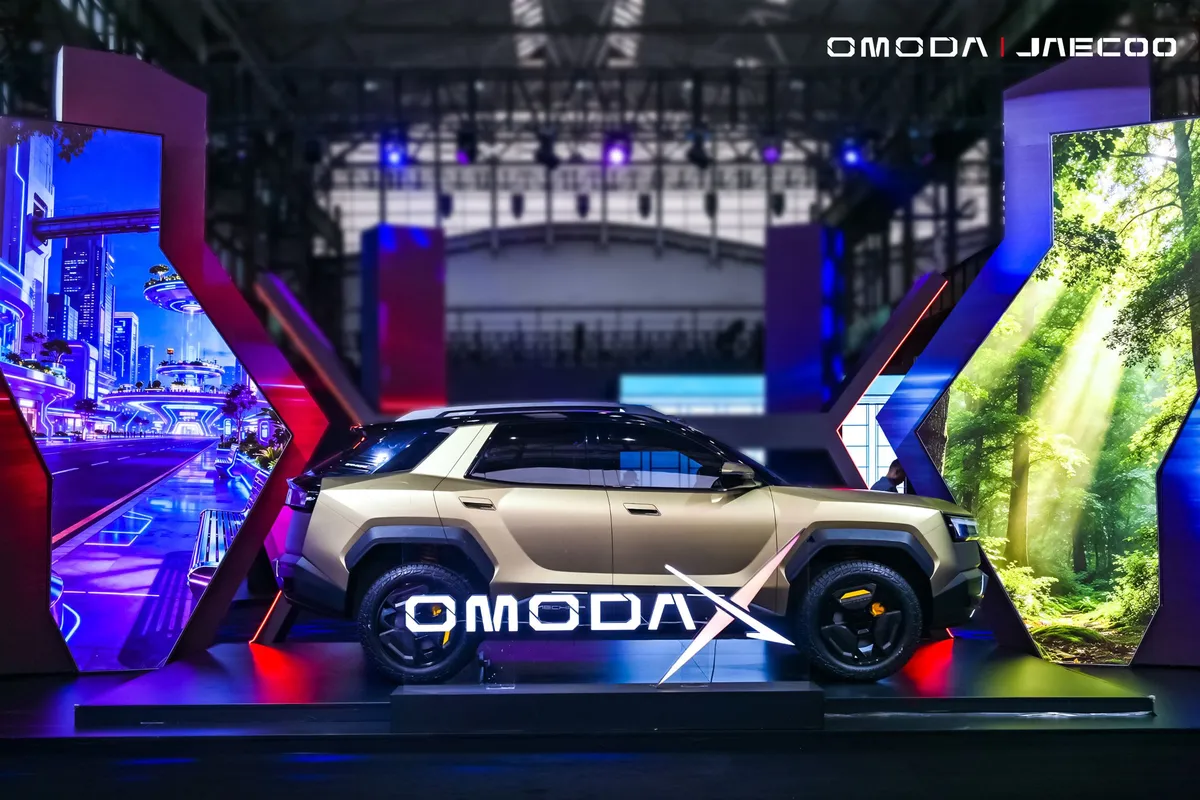 Heller Omoda X mit schwarzem Dach und schwarzen Rädern im Seitenprofil, davor ein großer leuchtender Omoda-X-Schriftzug.
