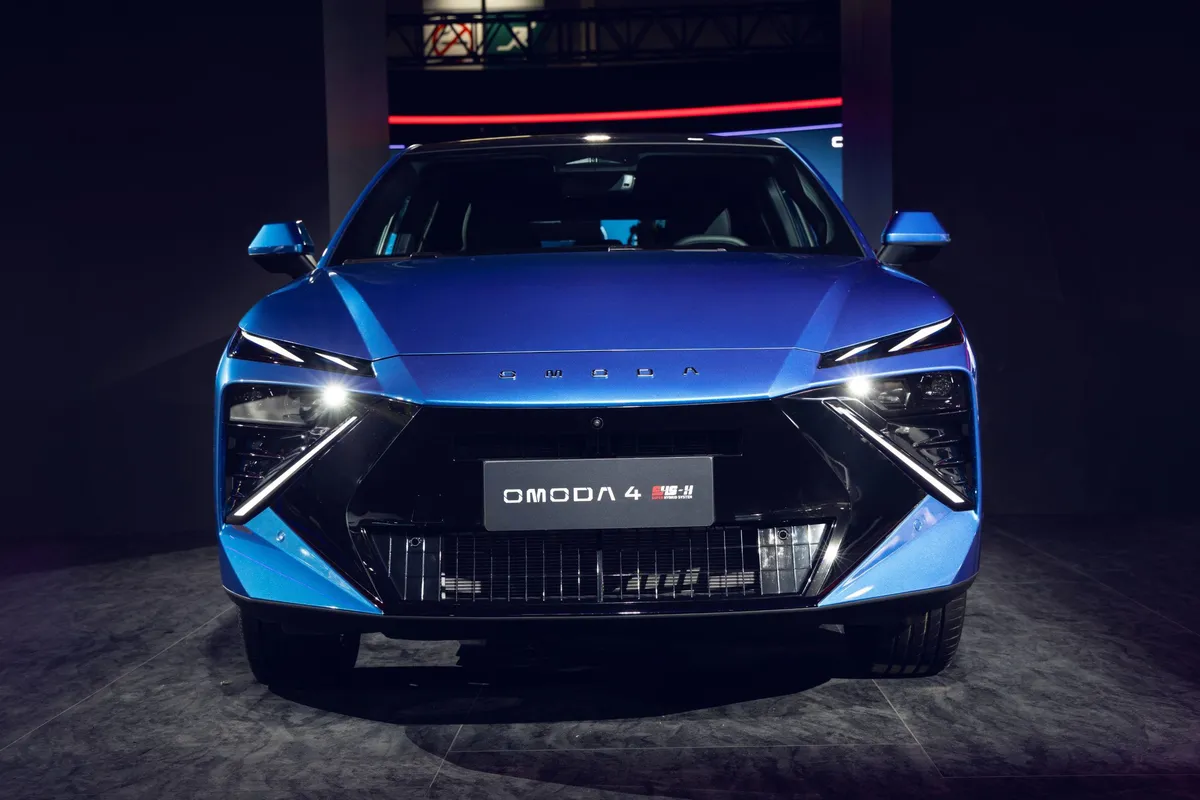 Blauer Omoda 4 frontal auf einem dunklen Messestand, gut sichtbar die schmalen Tagfahrleuchten und der große schwarze Frontgrill.