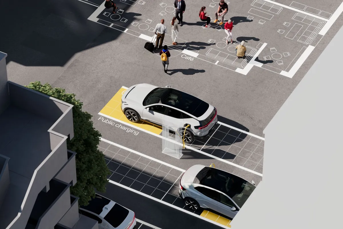 Luftaufnahme eines weißen Polestar 3, der über ein gelbes Kabel an einer öffentlichen Ladesäule auf einem gepflasterten Platz hängt.