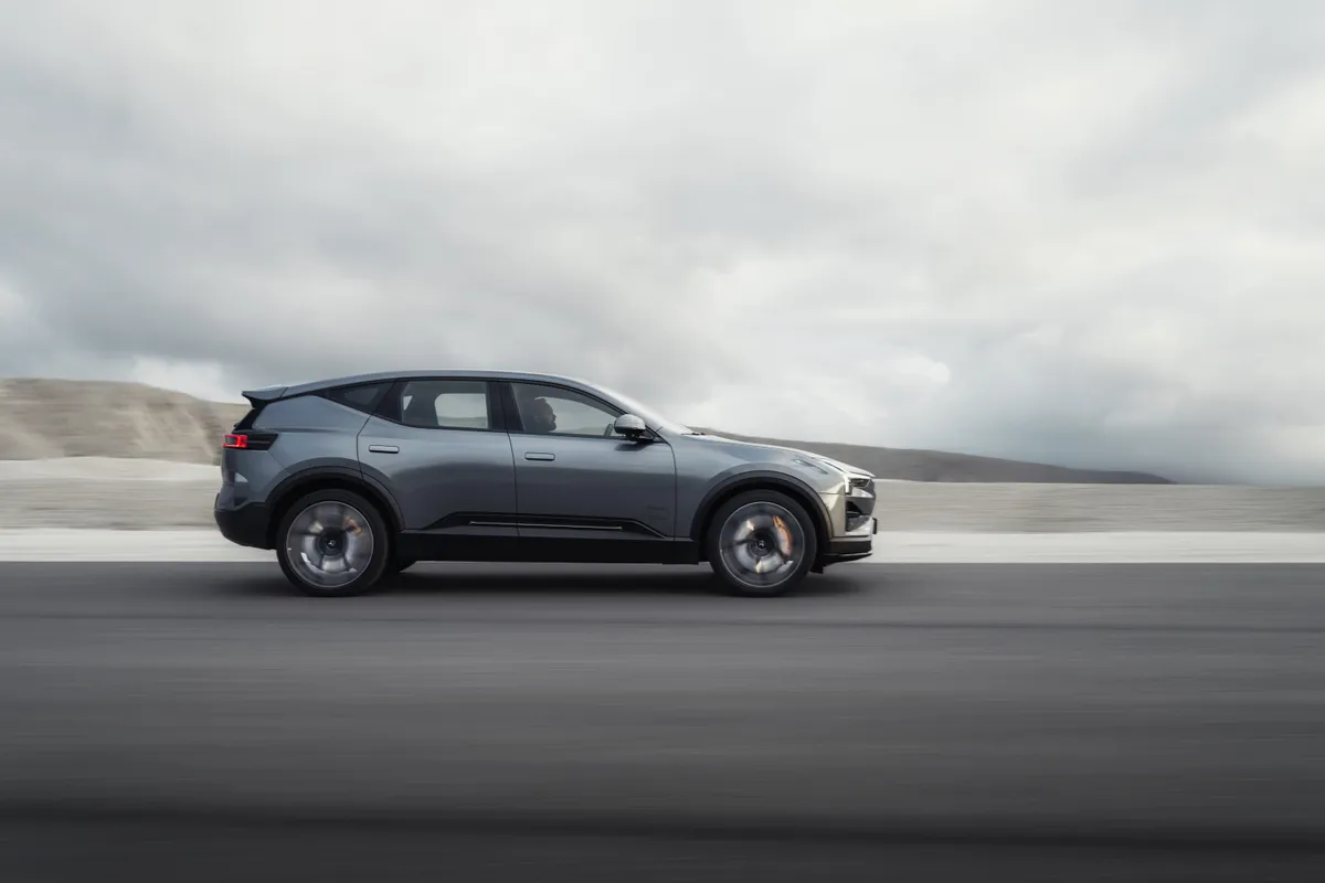 Grauer Polestar 3 in der Seitenansicht auf einer asphaltierten Teststrecke vor einer kargen, hellen Landschaft.