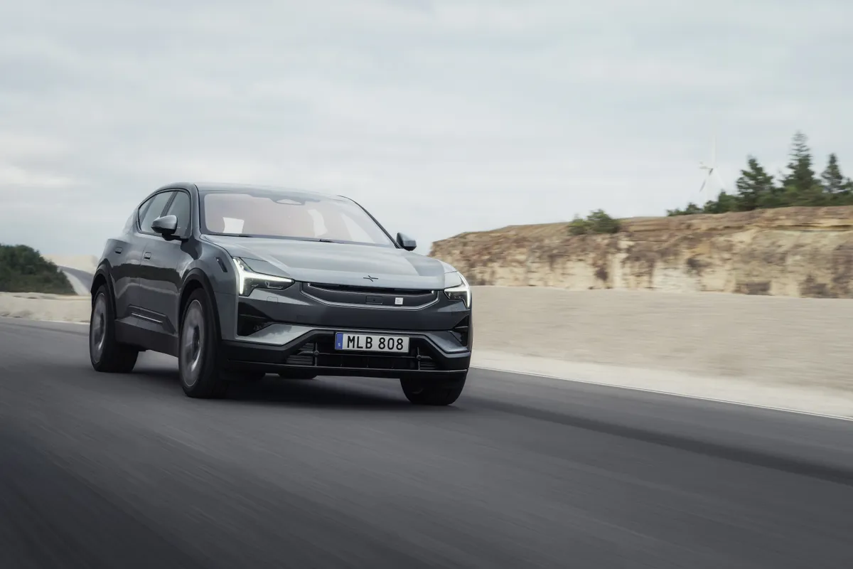 Dunkelgrauer Polestar 3 von schräg vorne auf einer Teststrecke an einer hellen Böschung mit einzelnen Bäumen.