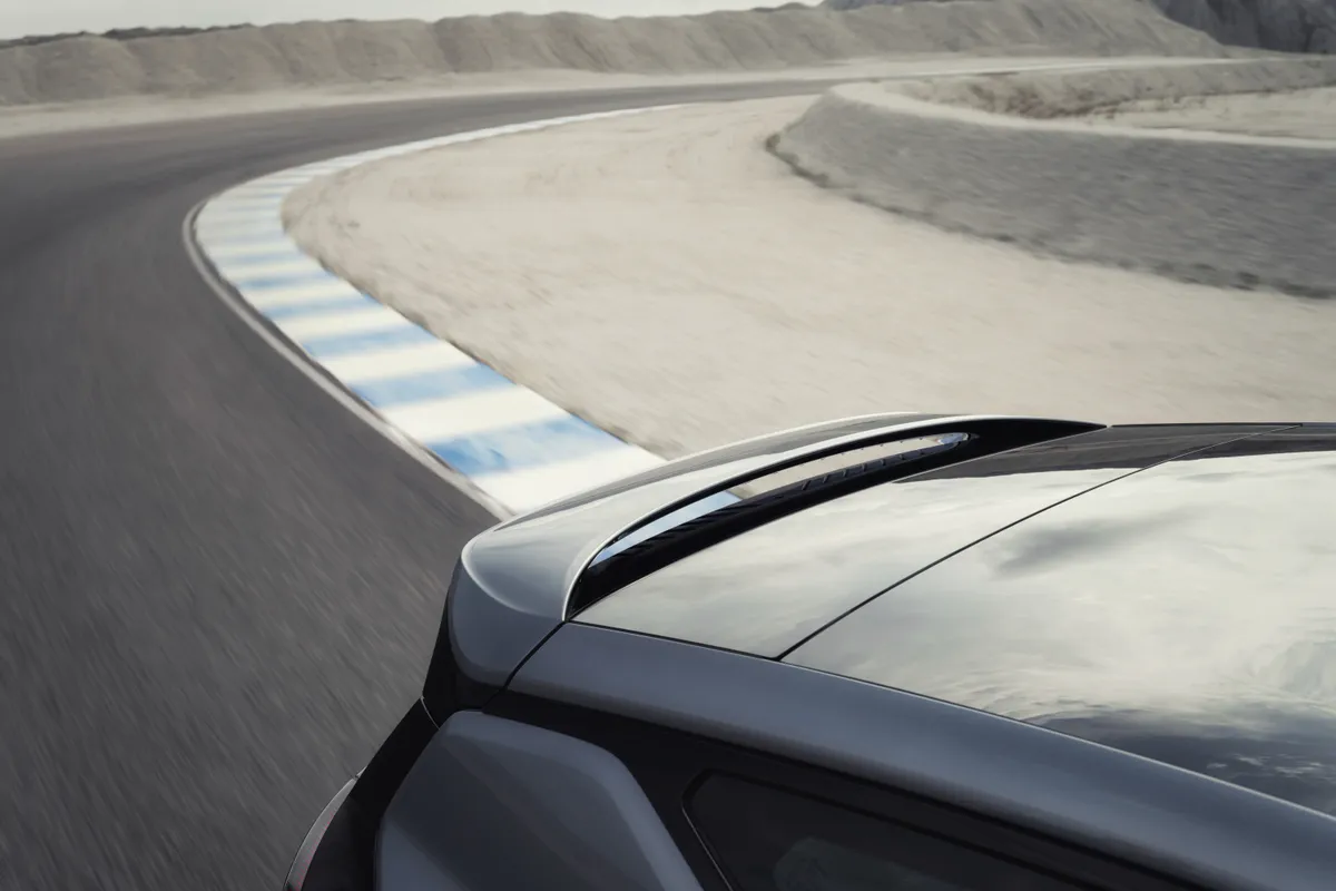 Ausschnitt der grauen Motorhaube eines Polestar 3 vor einer kurvigen Teststrecke.