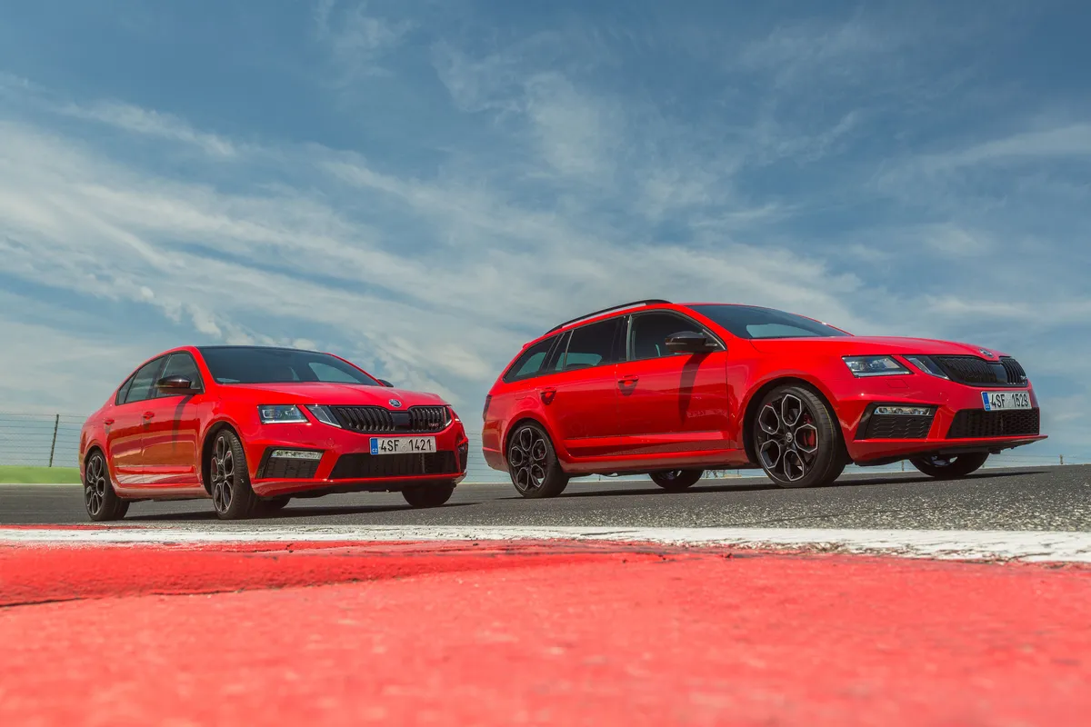 Zwei rote Škoda Octavia RS der dritten Generation, eine Limousine und ein Combi, auf einer Rennstrecke unter blauem Himmel.