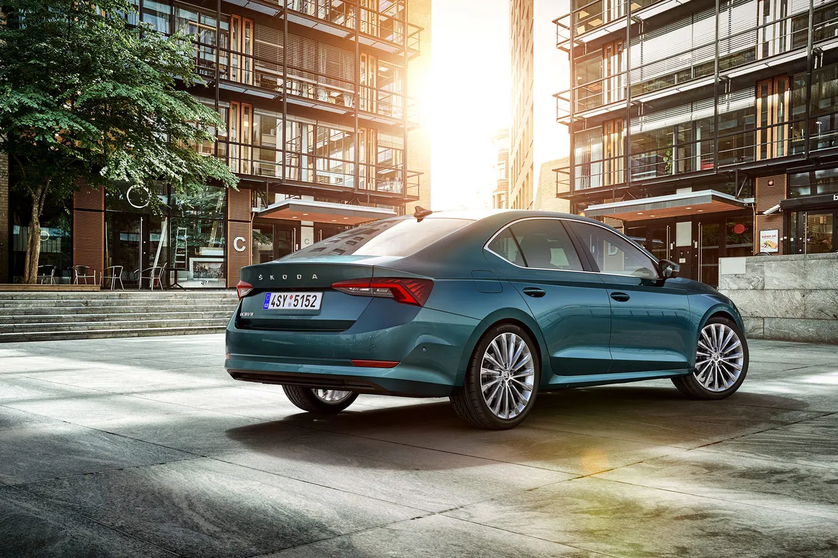 Petrolfarbener Škoda Octavia Limousine der vierten Generation von schräg hinten zwischen modernen Gebäuden im Abendlicht.