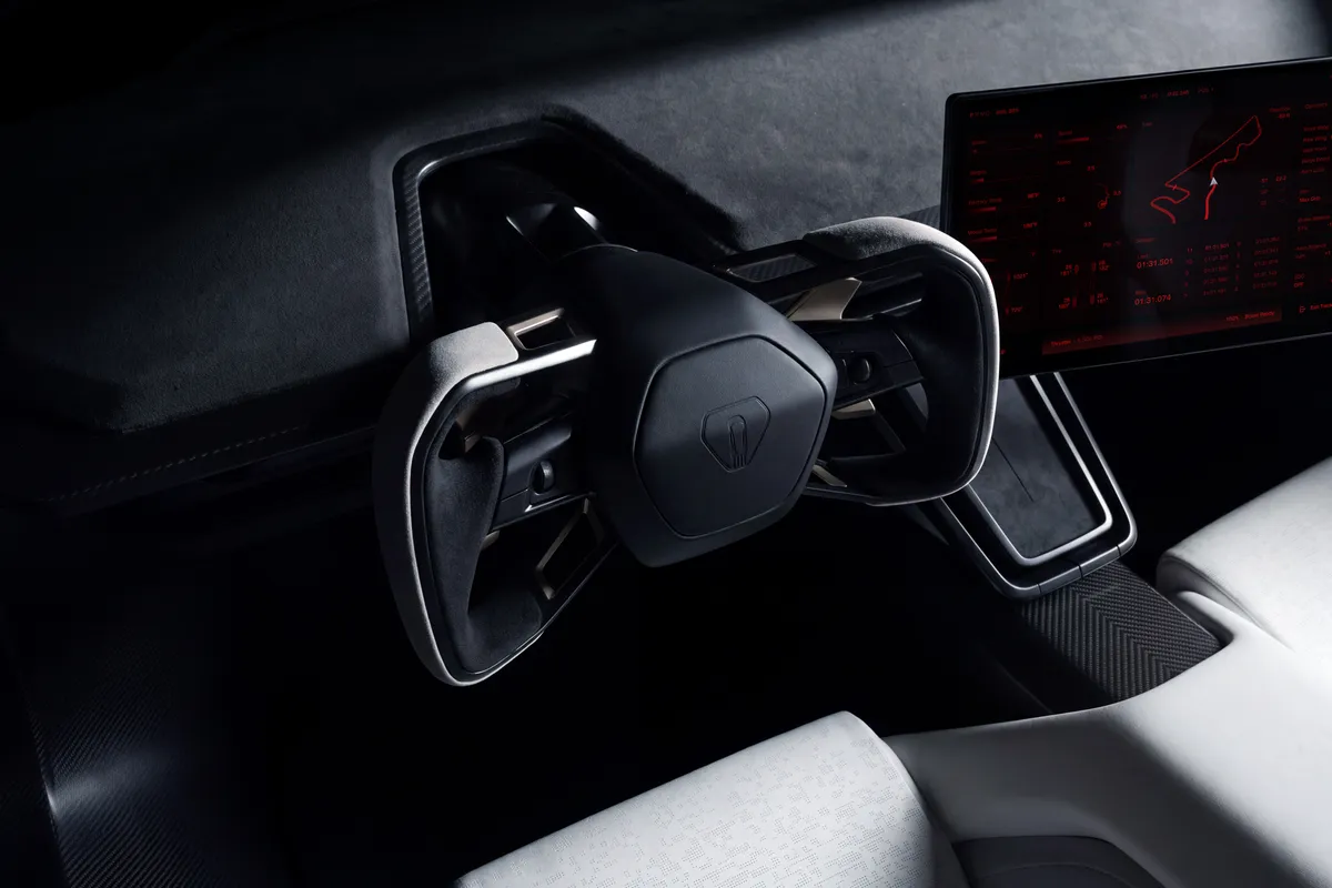 Dunkles Cockpit des Tesla Roadster mit offenem Lenkrad in Yoke-Form, großem Bildschirm mit Streckengrafik und hellem Sportsitz.