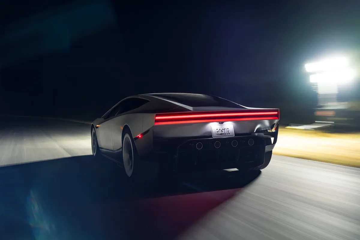 Silberner Tesla Roadster in Heck-Dreiviertelansicht bei schneller Nachtfahrt auf einer beleuchteten Strecke, mit rotem Rücklichtband.
