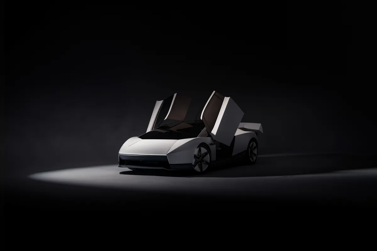 Silberner Tesla Roadster in Front-Dreiviertelansicht mit beiden nach oben geöffneten Türen im Lichtkegel vor schwarzem Hintergrund.