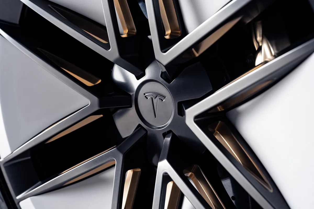 Nahaufnahme einer schwarz-silbernen, kantigen Leichtmetallfelge mit Tesla-Logo auf der Radnabe.