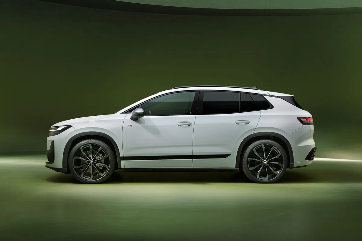 Weißer VW ID. Tiguan mit schwarzem Dach in der Seitenansicht vor grünem Studiohintergrund.