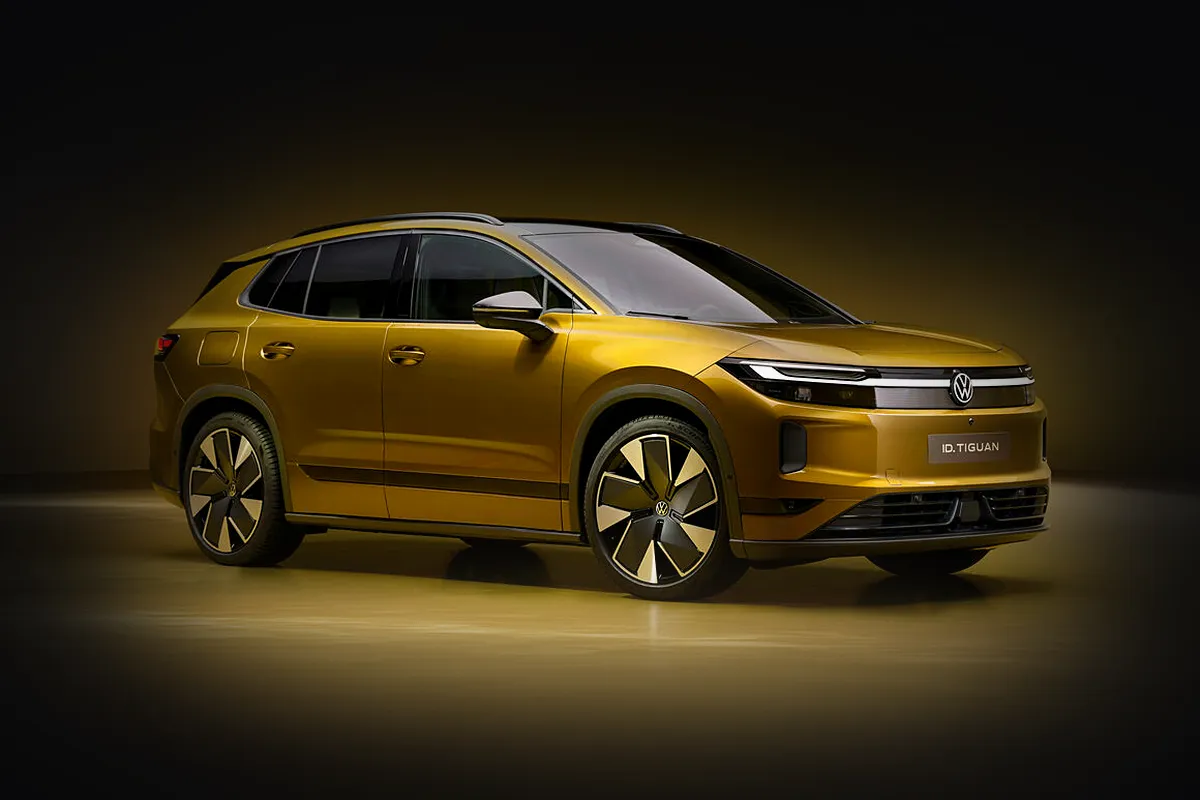 Goldfarbener VW ID. Tiguan von schräg vorne im warmen Scheinwerferlicht vor dunklem Studiohintergrund.