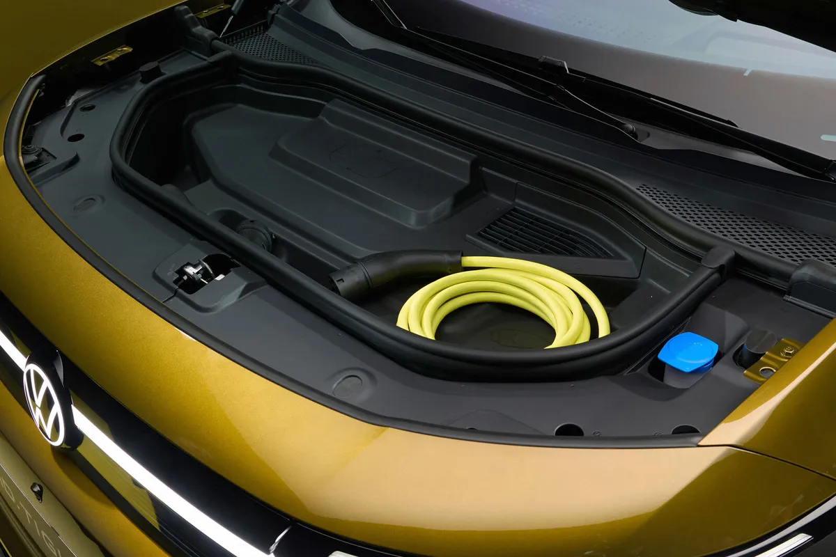 Der goldfarbene VW ID. Tiguan von schräg oben mit geöffneter Fronthaube; im Frunk liegt ein gelbes Ladekabel.