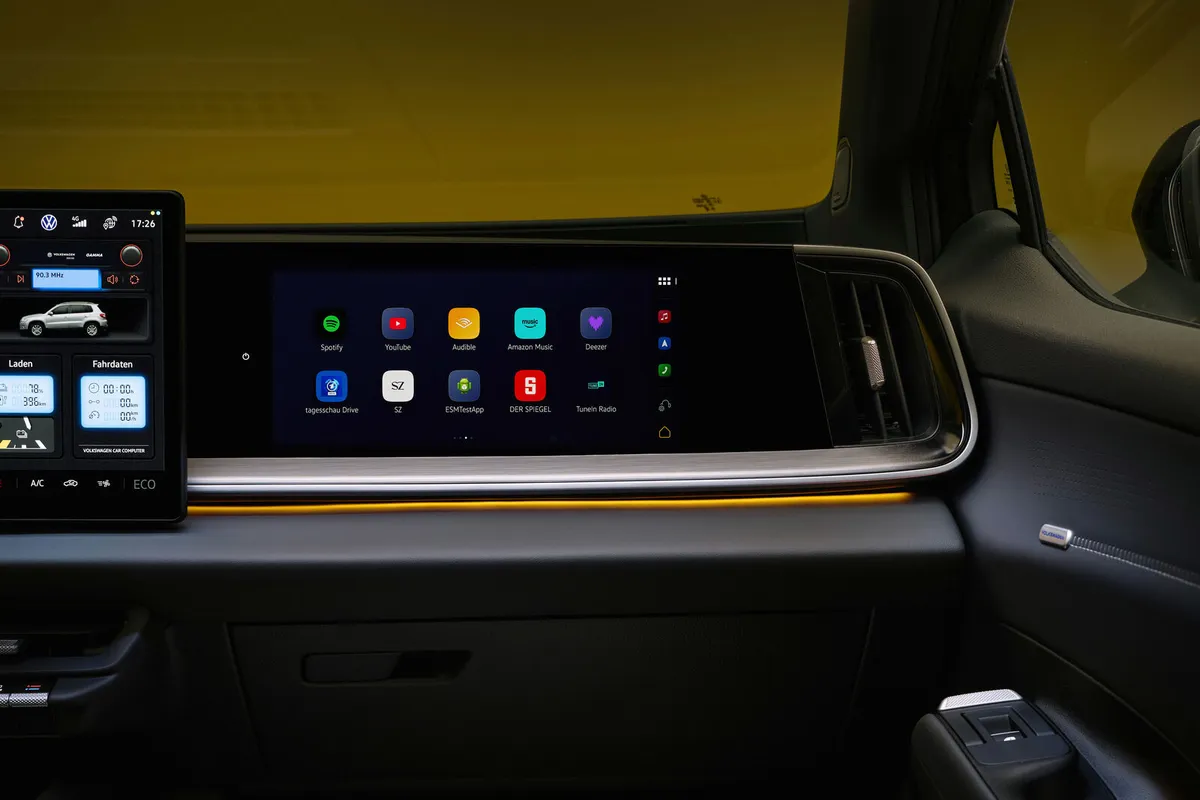 Armaturenbrett des VW ID. Tiguan auf der Beifahrerseite mit einem breiten Bildschirm, Lüftungsdüse und orangem Lichtband.