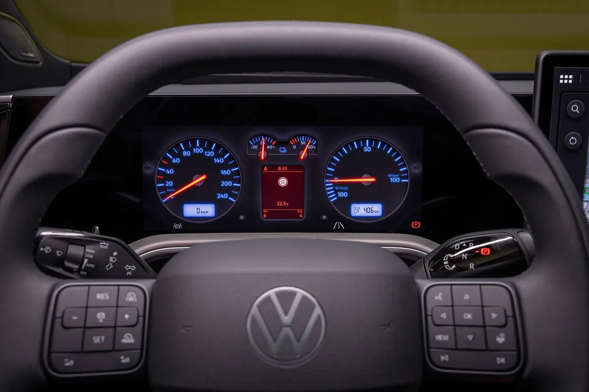 Lenkrad des VW ID. Tiguan mit physischen Tasten auf beiden Speichen, dahinter das Fahrerdisplay mit runden blauen Instrumenten und roten Zeigern.