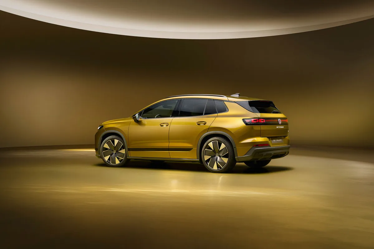 Der goldfarbene VW ID. Tiguan von hinten schräg links mit beleuchteten Rückleuchten.