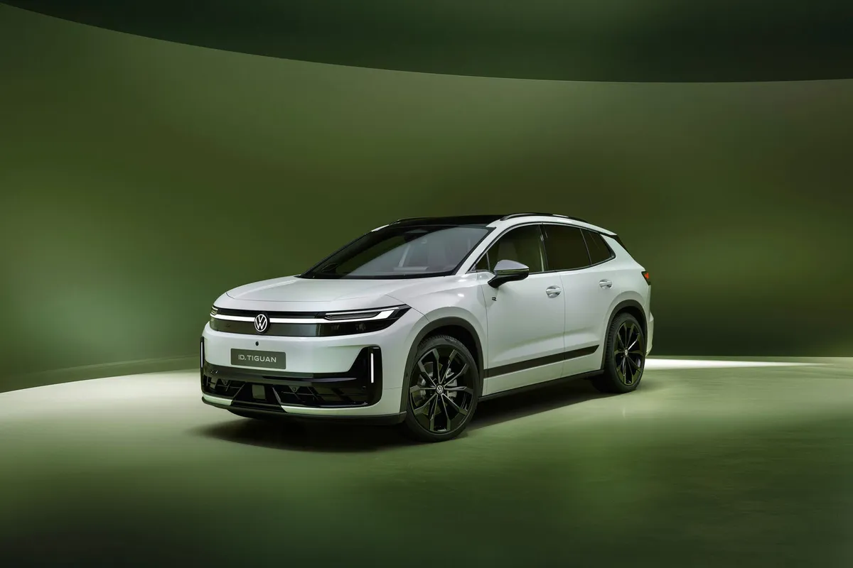 Weißer VW ID. Tiguan mit schwarzem Dach von vorne schräg links vor grünem Hintergrund.