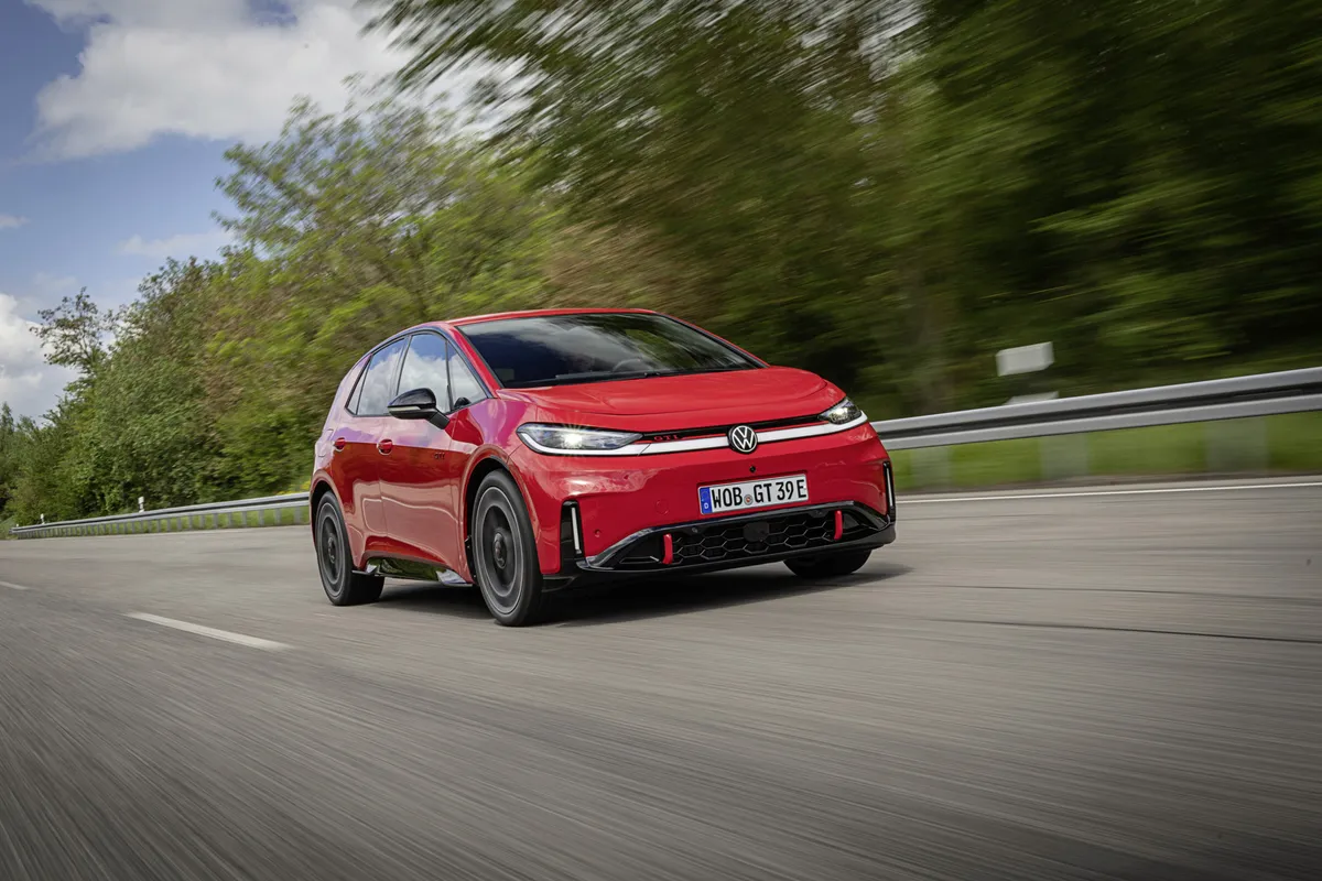 Roter VW ID.3 GTI fährt in vorderer Dreiviertelansicht auf einer mehrspurigen Straße, mit schwarzen Rädern und schmalem Lichtband, dahinter Bäume.