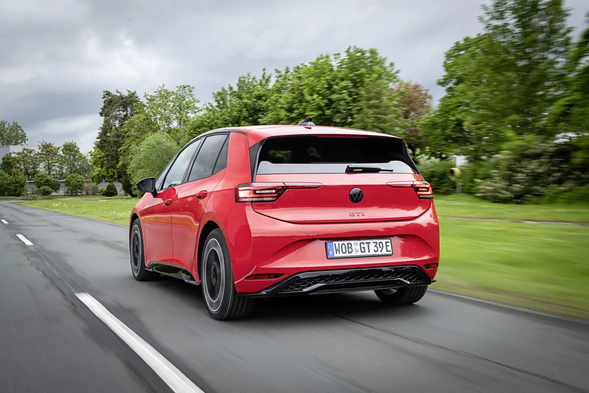 Roter VW ID.3 GTI von hinten auf einer von Bäumen gesäumten Straße, mit schwarzem Dachspoiler, schmalen Rückleuchten und GTI-Schriftzug.