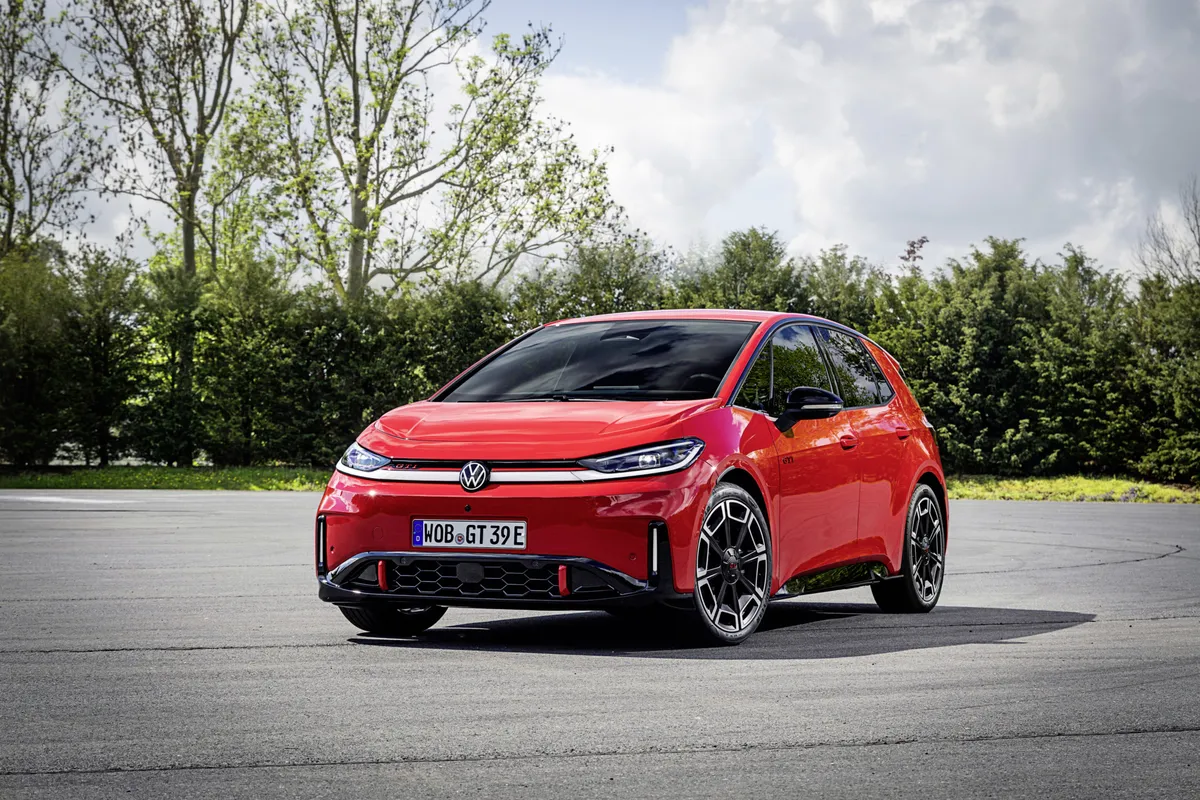 Roter VW ID.3 GTI steht in vorderer Dreiviertelansicht auf einer Asphaltfläche vor Bäumen, mit schmalem Lichtband und zweifarbigen Felgen.
