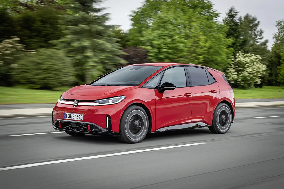 Fahrender roter VW ID.3 GTI von der Seite, Front und Flanke sichtbar, vor verwischten Bäumen und Leitplanke.