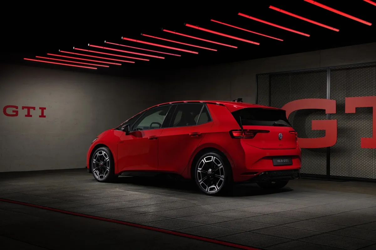 Roter VW ID.3 GTI von schräg hinten in einer dunklen Halle mit großen GTI-Schriftzügen an der Wand und roten Deckenleuchten.