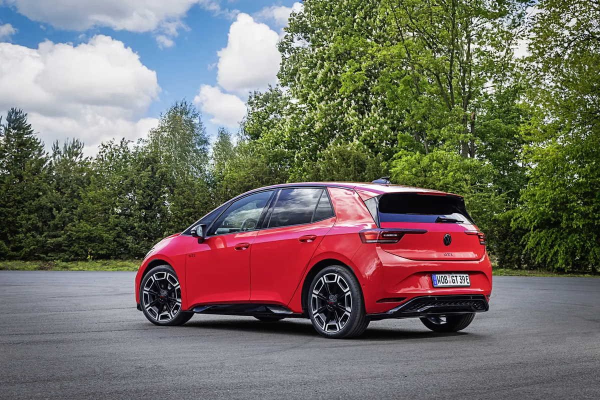 Roter VW ID.3 GTI in hinterer Dreiviertelansicht auf einer Asphaltfläche vor Bäumen, mit schmalen Rückleuchten und zweifarbigen Felgen.