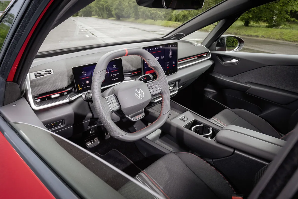 Blick durch die offene Fahrertür ins graue Cockpit des ID.3 GTI mit zwei Displays, roter Zierleiste und kariertem Sitzpolster.