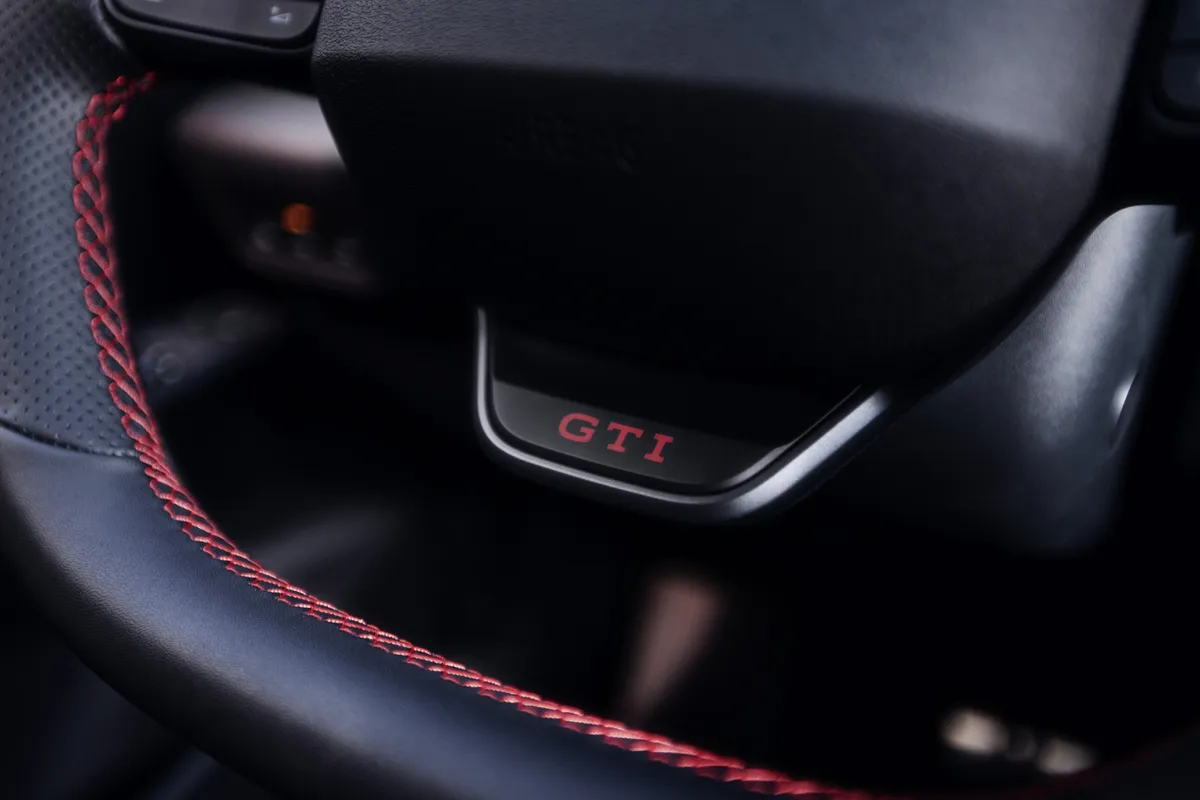 Nahaufnahme eines schwarzen Lenkrads mit perforiertem Bezug, roten Ziernähten und rotem GTI-Schriftzug auf der unteren Speiche.