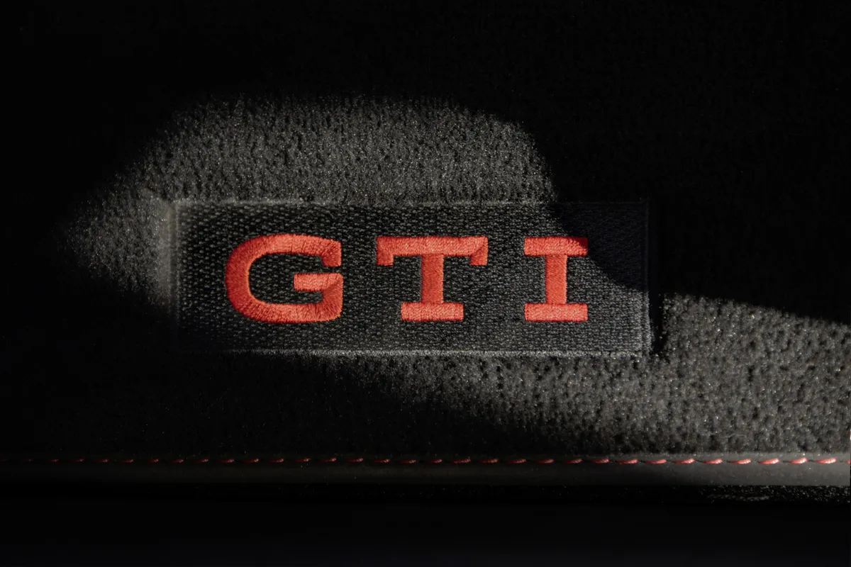 Nahaufnahme eines schwarzen Stoffbezugs mit rotem GTI-Schriftzug in schwarzem Rahmen und roter Ziernaht.