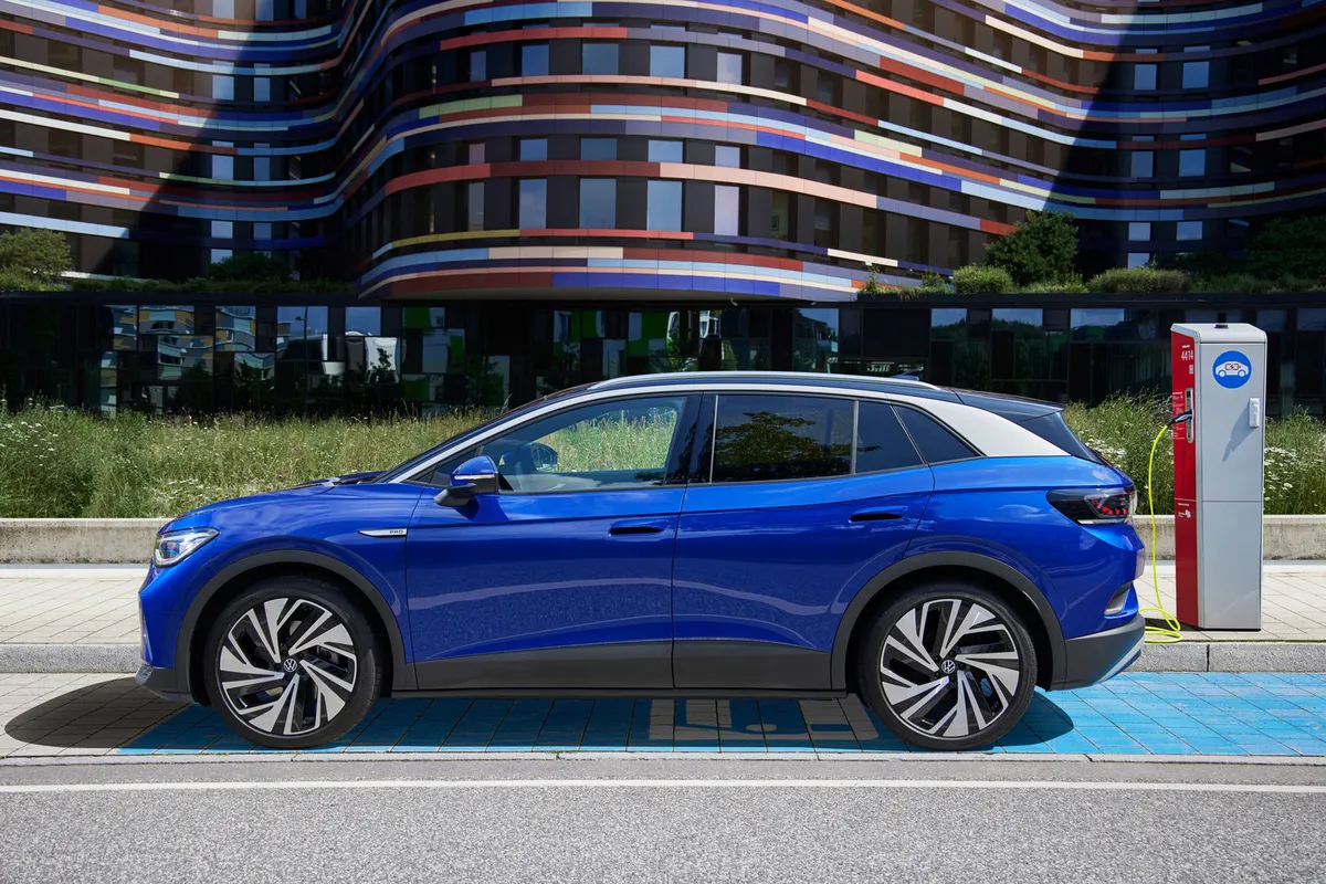 Blauer VW ID.4 im Seitenprofil in einer markierten Ladebucht vor einem bunten, modernen Gebäude.