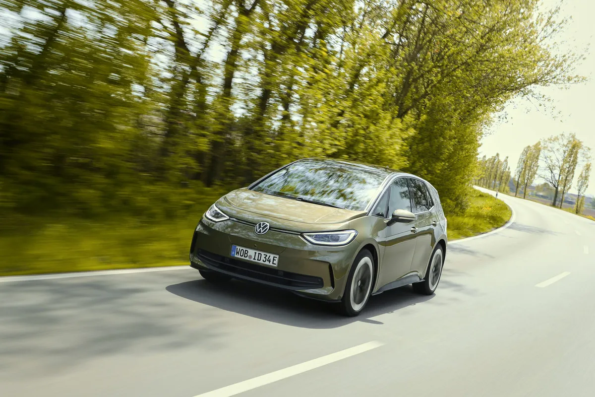 Olivgrüner VW ID.3 von schräg vorne in einer Kurve auf einer baumgesäumten Landstraße.