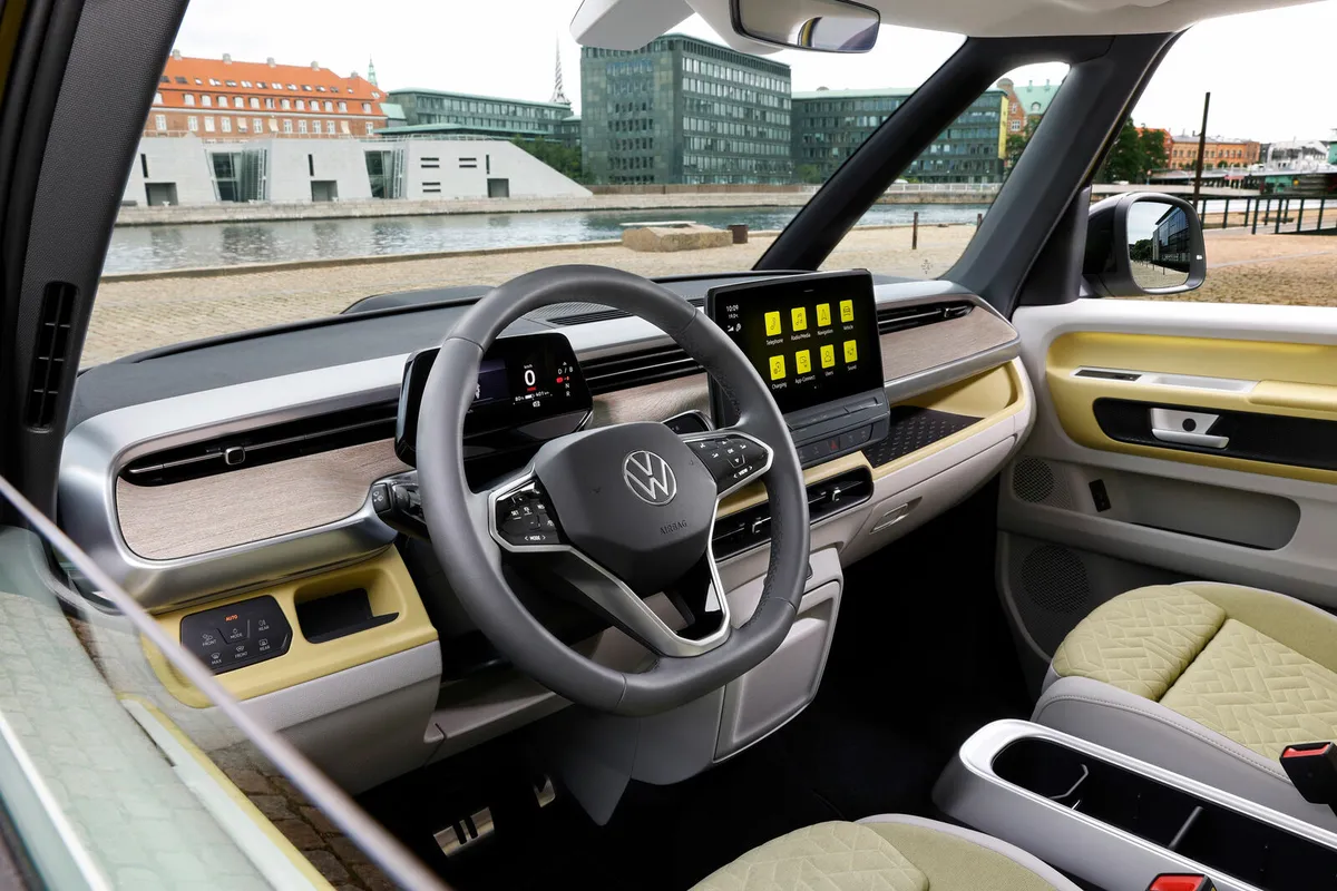 Innenraum des VW ID. Buzz mit grauem Lenkrad, gelben Akzenten am Armaturenbrett und Zentraldisplay.